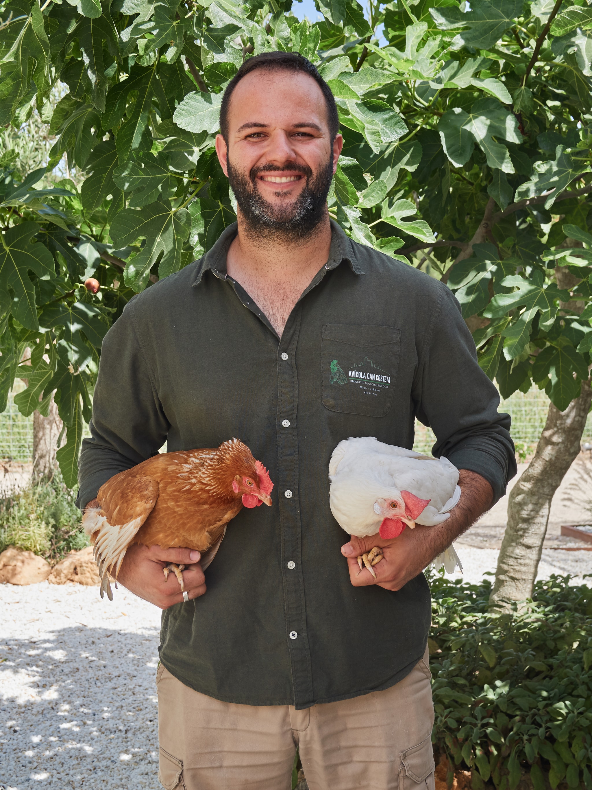 Un hombre de Can Costeta con dos gallinas en brazos delante de una higuera