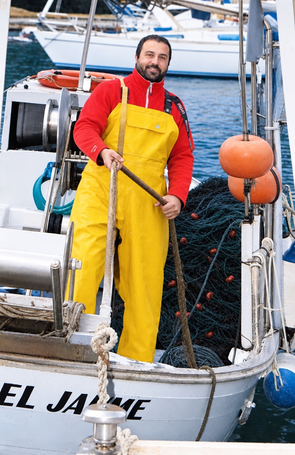 N'Andreu Gil a la proa de la barca Jaume, amb el pitet groc de pescador i les xarxes darrere