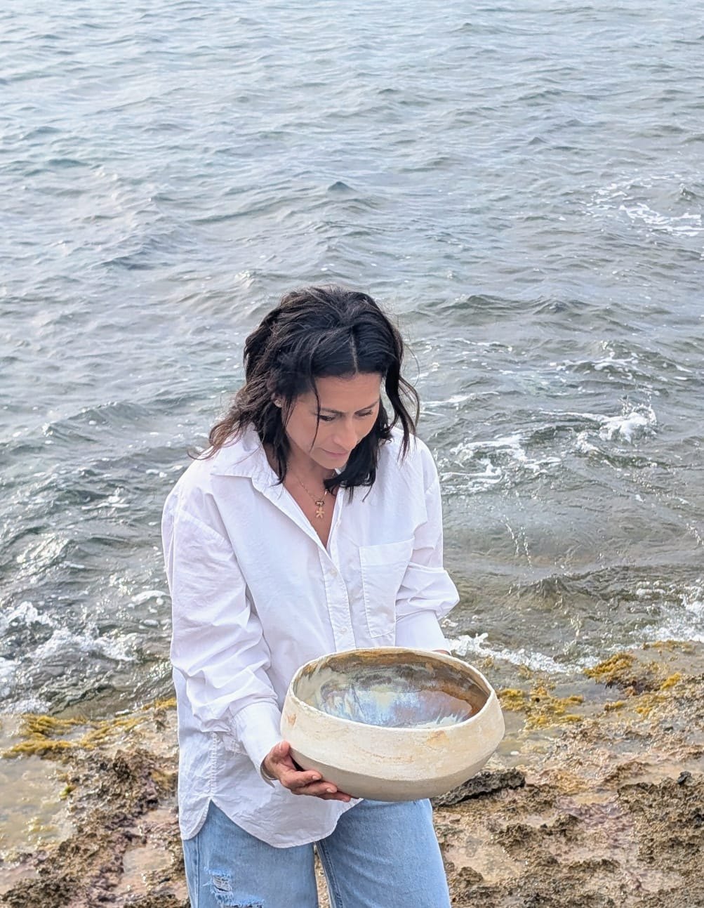 Carolina Arias junto al mar con un cuenco de barro en las manos